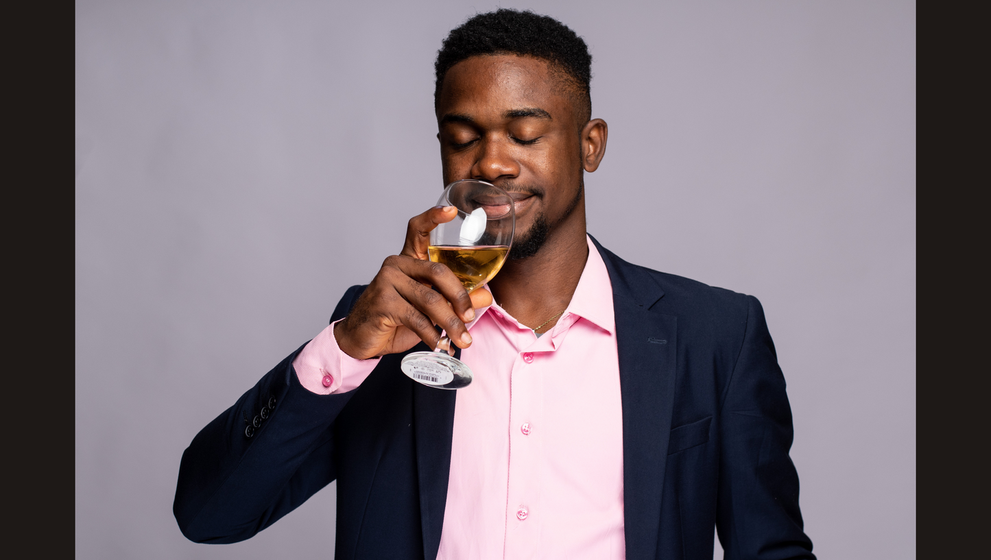Man in a suit and pink shirt holding a glass of white wine against a gray background